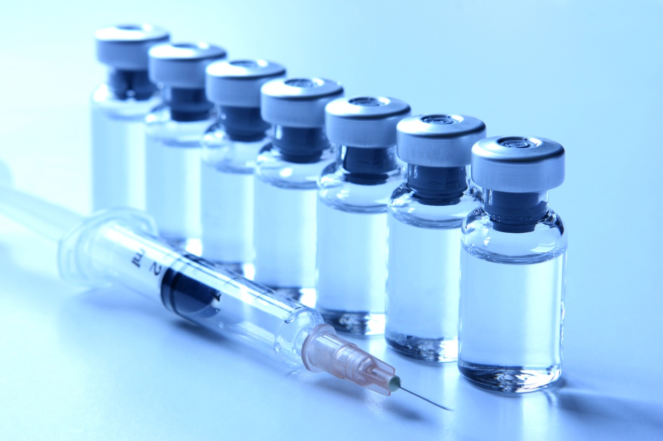Rows of clear glass vaccine vials with rubber stoppers.
